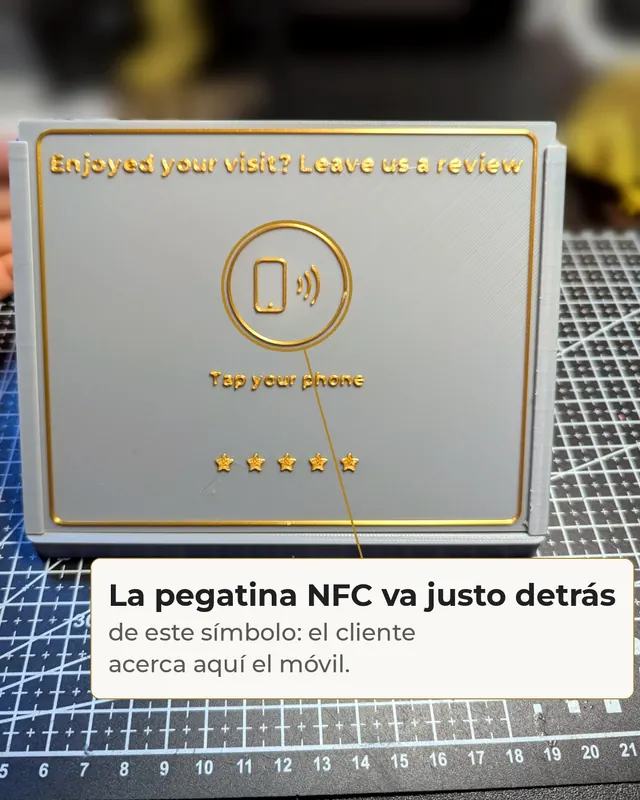 Stand gris con letras doradas y el símbolo NFC, con una nota que señala que la pegatina va justo detrás